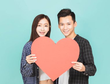 Kırmızı kalbi bir arada tutan genç çift mavi arka planda duruyor.