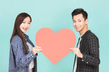 Kırmızı kalbi bir arada tutan genç çift mavi arka planda duruyor.