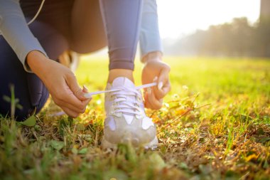 Kadın koşucu ayakkabılarını bağlıyor ve sabah koşuya hazırlanıyor.