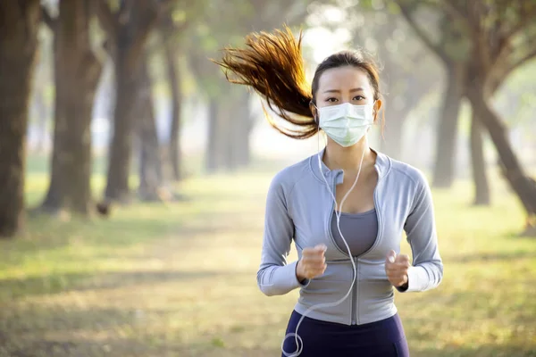 young woman in face mask and running in the park