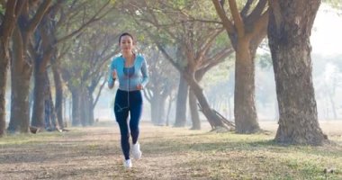 Güzel genç bir kadın sabah parkta koşuyor.