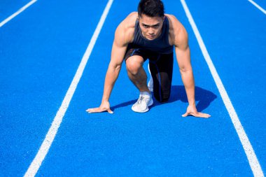 Yarış pistindeki Asyalı erkek sporcu koşmaya hazır.