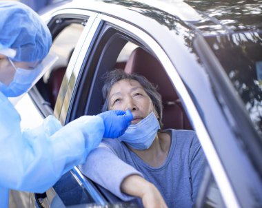 Doktor, yaşlı kadından olası koronavirüs enfeksiyonu testi için burun çubuğu alıyor.