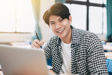 Genç neşeli Asyalı öğrenci sınıfta okuyor.