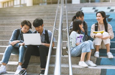 Mutlu genç öğrenciler konuşuyor ve merdivenlerde oturuyor. 