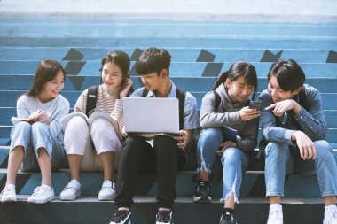 Mutlu genç öğrenciler konuşuyor ve merdivenlerde oturuyor. 