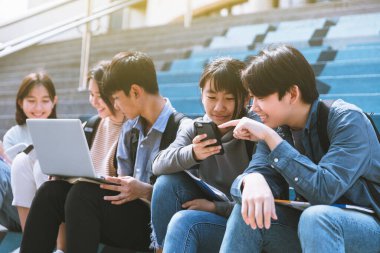 Mutlu genç öğrenciler konuşuyor ve merdivenlerde oturuyor. 