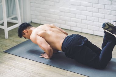 Kaslı Asyalı genç adam evde yerde egzersiz yapıyor.