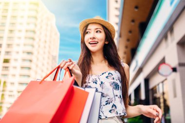 Genç ve çekici Asyalı kadın sokakta alışveriş torbaları tutuyor.