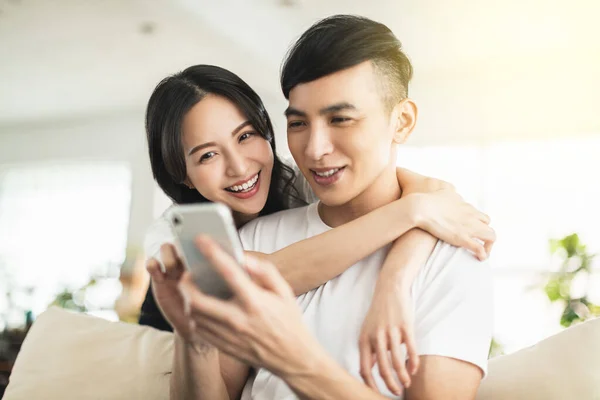 Evdeki Oturma Odasında Cep Telefonuna Bakarken Kucaklaşan Mutlu Genç Çift — Stok fotoğraf