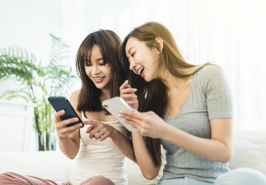 Evdeki kanepede oturan genç ve mutlu bir kadın akıllı telefonlarını kullanıyor.