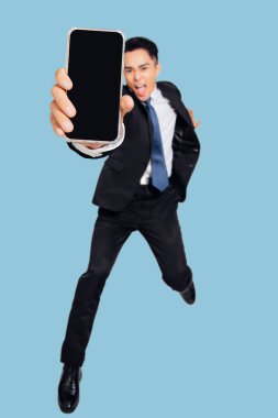 Heyecanlı genç iş adamı dans ediyor ve cep telefonu ekranını gösteriyor.