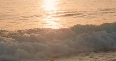 Gün batımında sahilde okyanus dalgaları. Güneş ışığı su yüzeyine yansıyor.