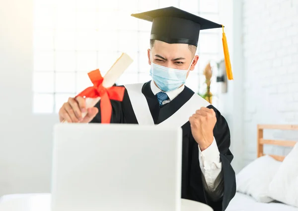 快乐的大学生 戴着医疗面具 坐在办公桌前 拿着笔记本电脑 拿着毕业文凭 庆祝成功 — 图库照片