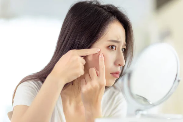 Young woman looking at  mirror and checking the  acne problem at home