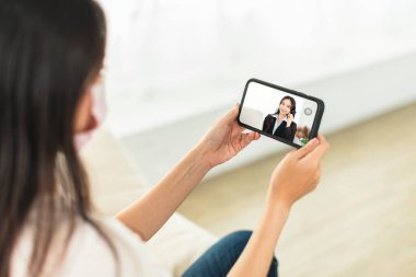 Genç kadın kendini korumak için maske takıyor ve şirketteki iş arkadaşlarıyla video görüşmeleri yapıyor.