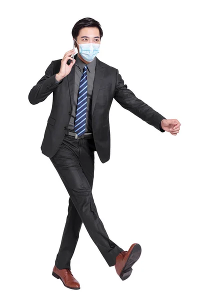 若いビジネスマンが携帯電話で話し白い背景に隔離された保護医療マスクをつけて歩く — ストック写真