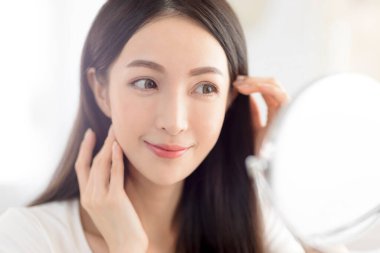 Genç kadın elleri tenine dokunuyor ve aynaya bakıyor.