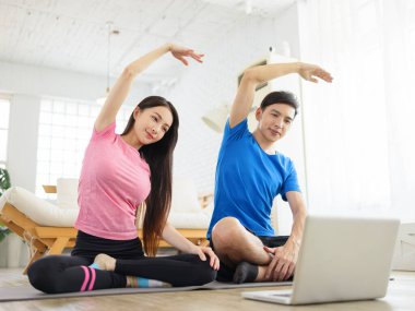 Evde egzersiz yapan, spor minderinde oturan ve dizüstü bilgisayarda video izleyen sağlıklı bir çift..