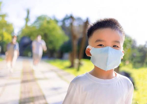 快乐的小男孩戴着医疗面具 和父母一起在公园里散步 — 图库照片