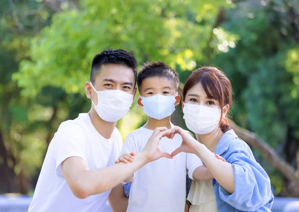 Happy family wearing protective medical masks for protection from covid-19 and  showing hand heart gesture