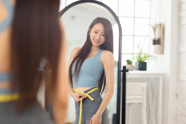 年轻女子用带子测量腰围 站在镜子前 体重减轻概念 — 图库照片