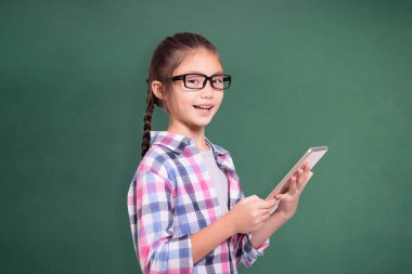 Tablet kullanan mutlu öğrenci kız. Yeşil karatahta arka planda izole edilmiş..