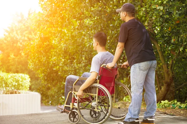 Jeune homme assis sur un fauteuil roulant avec son frère — Photo