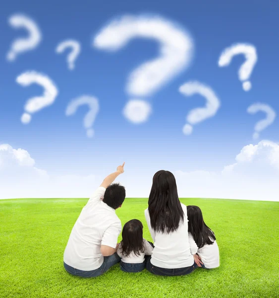 Familia feliz sentado en un prado con la consulta de las nubes — Foto de Stock