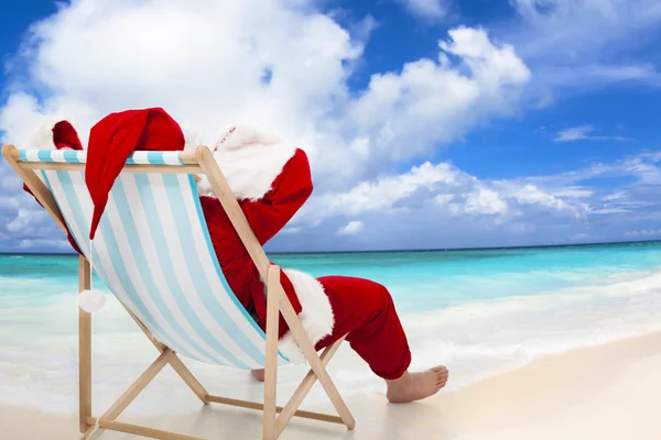 Santa claus zittend op het strandstoelen met blauwe hemel en cloud — Stockfoto