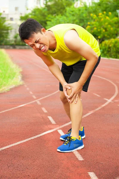 Corredor masculino joven que sufre de lesión de rodilla en la pista —  Fotos de Stock