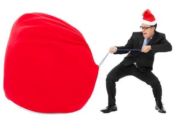 Business man carrying a heavy gift sack with christmas hat — Stock Photo, Image