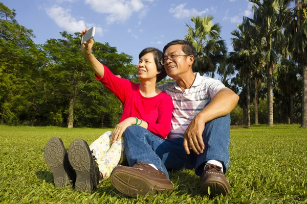 Старшая азиатская пара сидит на лугу и фотографирует — стоковое фото