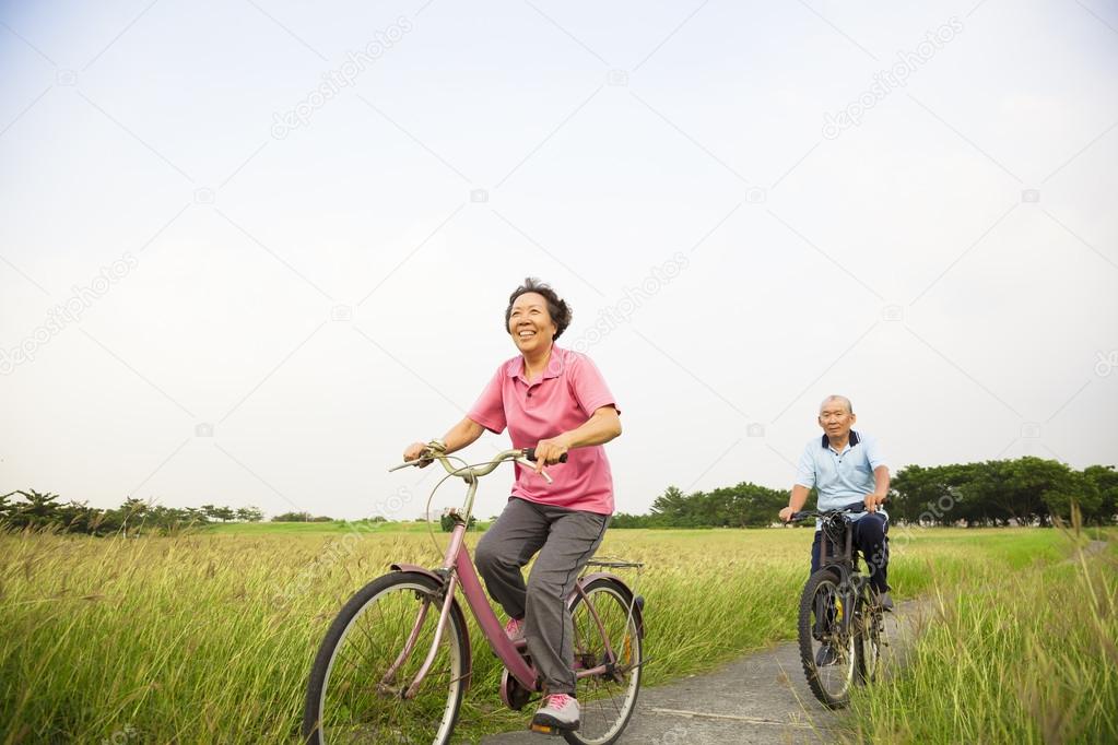 Happy Asian elderly seniors couple biking in the park with blue 