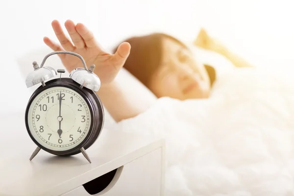 Young Woman turning off the alarm clock on the bed — Stock Photo, Image