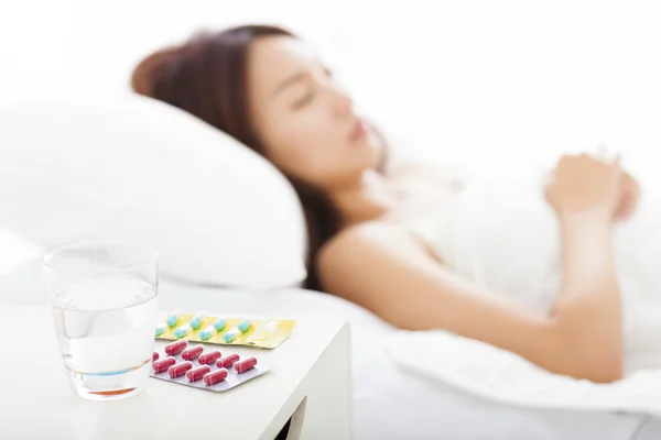 Medicinali e acqua di fronte, donna beccata a dormire fredda a letto — Foto Stock