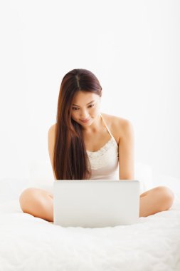 güzel genç Asyalı kadın yatakta dizüstü bilgisayar kullanarak