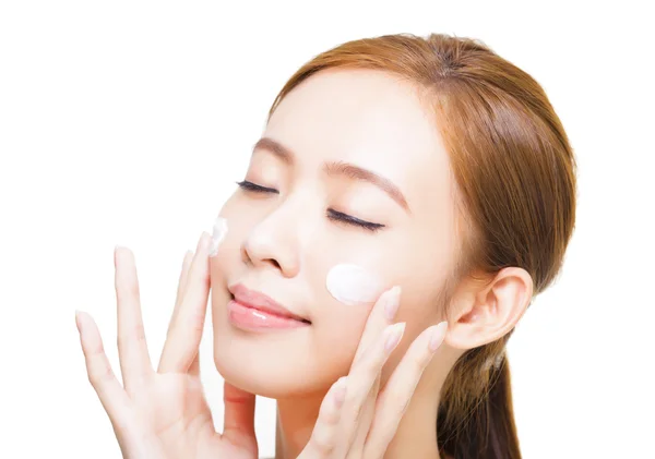 Bella giovane donna applicando crema cosmetica sul suo viso — Foto Stock