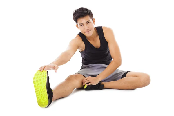 Sonriente joven fitness hombre sentado y haciendo ejercicio de estiramiento — Foto de Stock