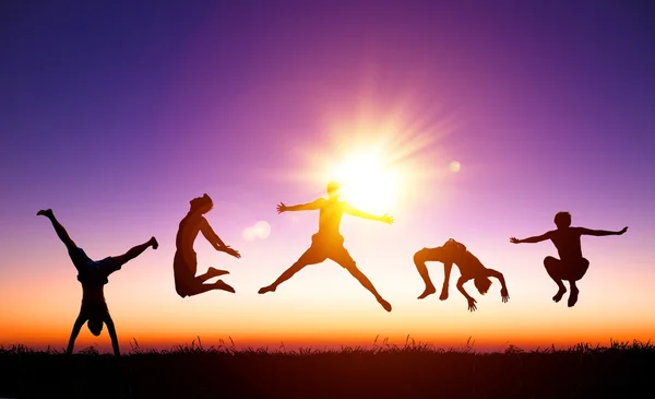 Jóvenes felices saltando en la colina con luz del sol de fondo — Foto de Stock