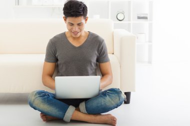 kanepe oturma ve dizüstü bilgisayar kullanarak mutlu genç adam