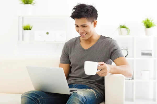 Glad ung Man sitter i soffan och använder bärbar dator — Stockfoto