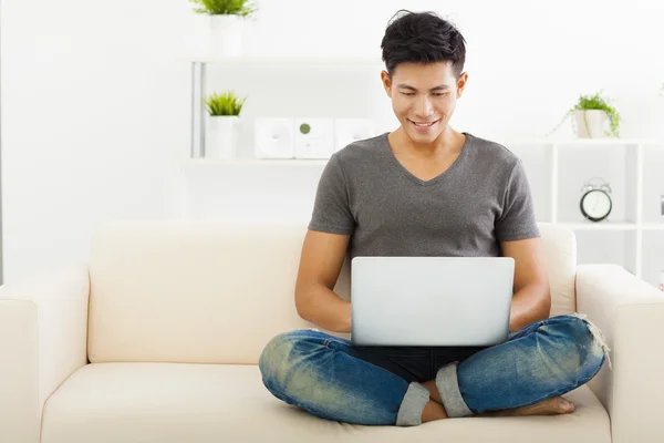 Ung Man sitter i soffan och använder bärbar dator — Stockfoto