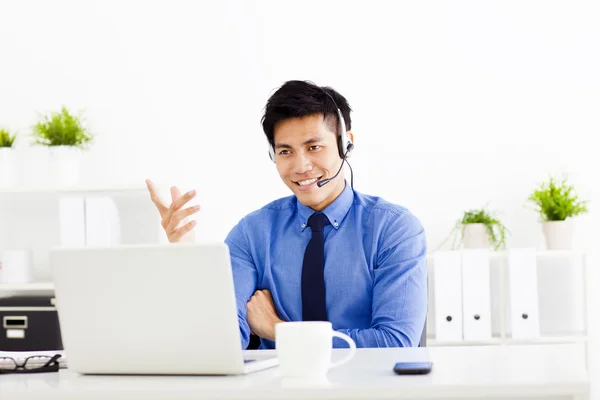 Homem de negócios sorrindo usando um fone de ouvido no escritório — Fotografia de Stock