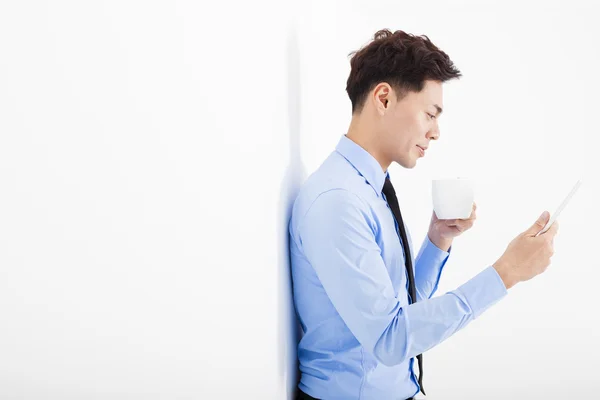 Joven empresario sosteniendo la tableta y apoyado contra la pared blanca — Foto de Stock