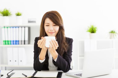 Güzel genç iş kadını ofiste kahve içiyor.