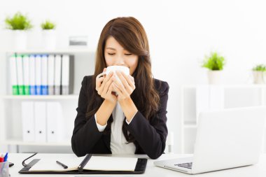 Güzel genç iş kadını ofiste kahve içiyor.