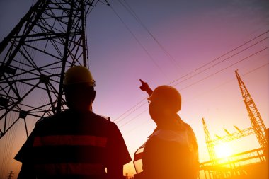 two worker watching the power tower and substation with sunset b clipart