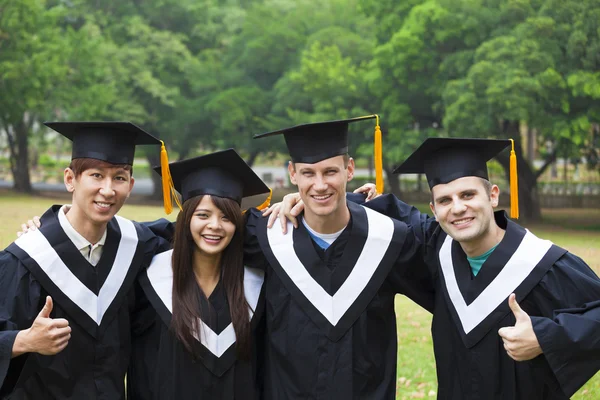 Happy students in graduation gowns on university campus — Stock Photo, Image