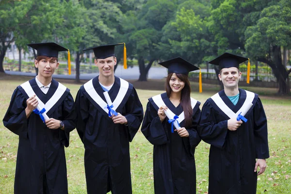 Estudantes felizes em vestidos de formatura no campus universitário — Fotografia de Stock